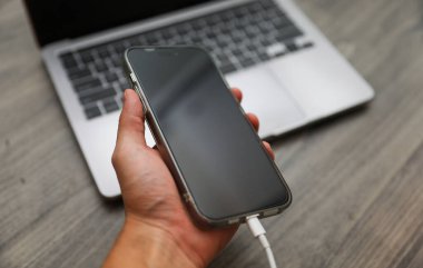ahşap masada şarj aleti olan akıllı telefonu tutan..