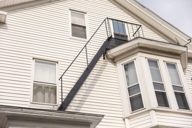 Beyaz ahşap balkon. Evin önünde iki pencere ve merdiven var.