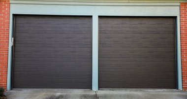 Kahverengi metal garaj kapısı, binanın ön cephesinde beyaz boya, gri bir duvar ve kapı..