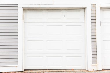 Beyaz ahşap garaj kapısı, beyaz duvar ve arka planda gri tuğla duvar..