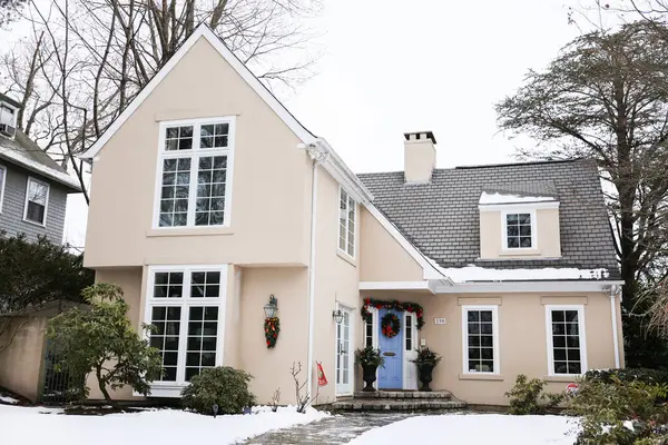 Kışın karlı ağaçları ve kırmızı tuğlalı duvarı olan beyaz bir ev.