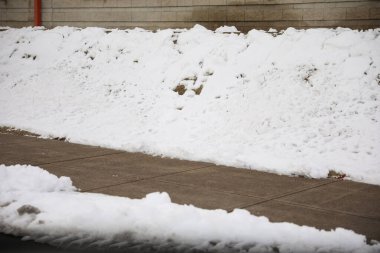 Önünde karlar ve ağaçlar olan şehir parkında karla kaplı bir kaldırım..