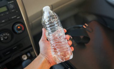 Kadın elinde plastik bir şişeyle masada bir araba tutuyor.