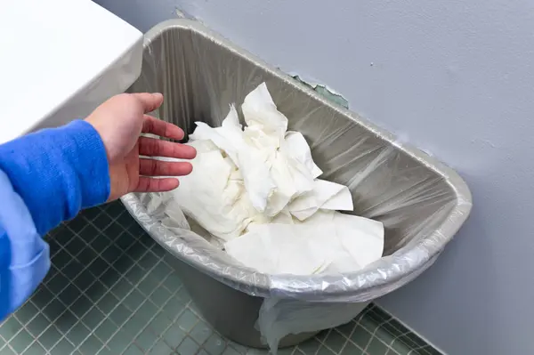 Banyodaki beyaz bir tabakta beyaz bir tuvalet kağıdı ve el..