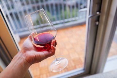 Kadın elinde bardakla kırmızı şarap tutuyor.