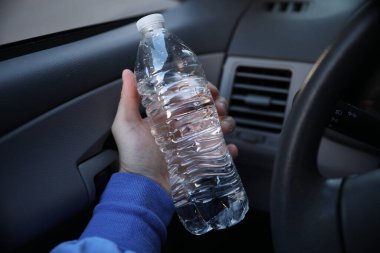 Siyah arka planda su olan plastik bir şişeyi tutan adam.