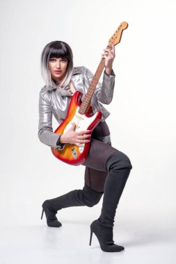 Güzel bir kadın seksi bir elbise ve beyaz arka planda elektro gitar tutan çizmeler giyiyor.