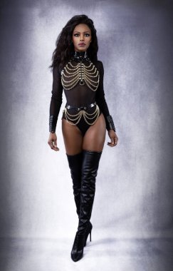 Beautiful sexy black dominant woman in leather chain harness outfit and thigh high boots posing full length in studio on gray mottled background clipart