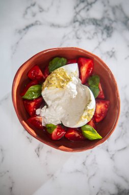 Burrata peynirinden, olgun domateslerden ve kil bir kasede kokulu fesleğenden oluşan rustik bir kompozisyon..