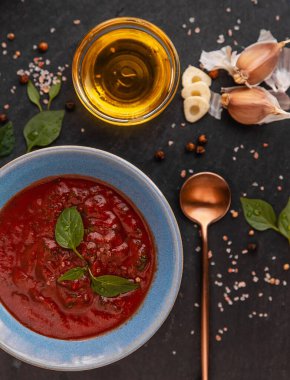 Siyah biberli domates sosu, sarımsak, zeytinyağı ve lacivert bir tabakta koyu renkli fesleğen yaprakları.
