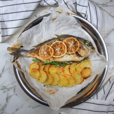 Kızarmış Dorado balığı ve patates dilimleri mermer bir masada metal tepside garnitür olarak kullanılıyor.