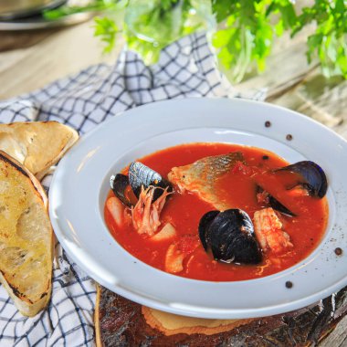 Köy ahşap bir masada beyaz bir tabakta deniz ürünleri domates çorbası kareli peçete ve kızarmış ekmek.
