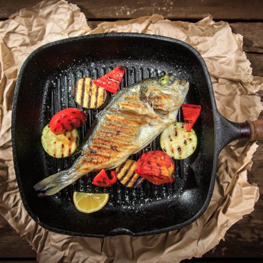 Izgara Dorado balığı ve garnitürlü sebzeler. Izgara tavada, kraft kağıdının üzerinde duruyor.