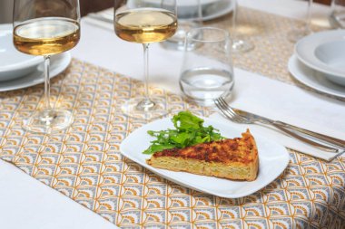 Bir parça klasik Lauren quiche roka ile servis edilir bıçak ve çatalla ile bir bardak su ve şarap ile