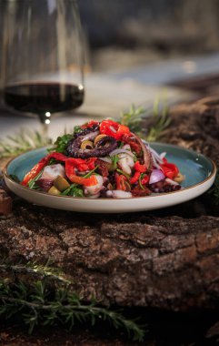 Ahtapot dokunaçlı salata ve ahşap ve ağaç kabuğundan yapılmış yeşil bir tabakta şarap sosunda karışık sebzeler.