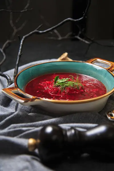 red beet soup with homemade sour cream sauce in a blue plate stands on a gray napkin on a black table, next to a garlic and black pepper shaker