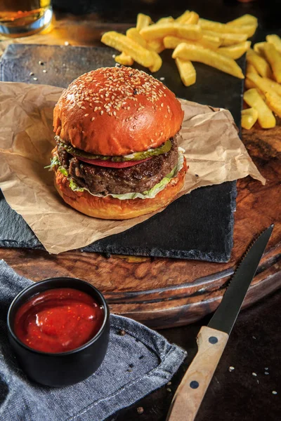 burger with meat cutlet, cheese and fries on craft paper on a dark background