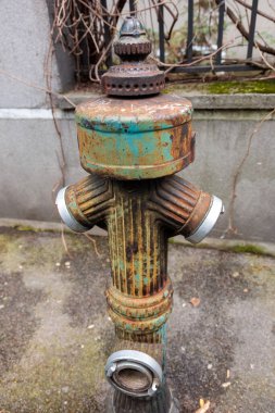 Görüntü caddeye kurulmuş bir yangın musluğunu gösteriyor. Yangın musluğu kırmızıya boyanmış ve yangın hortumlarını bağlamak için iki hortumu var. Yangın musluğunun kapağı kapalı ve vücut su kaynaklarını kontrol etmek için vanaları gösteriyor.. 