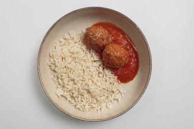 Zengin domates sosuna buharda pişirilmiş beyaz pirinçle seramik kasede servis edilen yumuşak köftelerin üst görüntüsü. Yemek fotoğrafçılığı, tarif blogları ve konforlu gıda projeleri için ideal.
