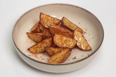 Kırmızı biber soslu ve seramik tabakta yağ parlatıcısı olan kızarmış patates dilimlerinin yakın plan çekimi. Yemek fotoğrafçılığı, tarif blogları ve konforlu yemek özellikleri için ideal.