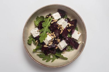 Kavrulmuş pancar kökü küpleri, kremalı feta peyniri, taze roka yaprakları, ayçiçeği çekirdekleri ve seramik kasede mikro yeşillikler içeren canlı pancar salatası. Sağlıklı beslenme, yemek blogları ve yemek fotoğrafçılığı için mükemmel.. 