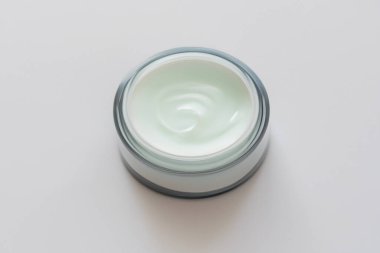 Beyaz arka planda cam bir kavanozda kozmetik krem.