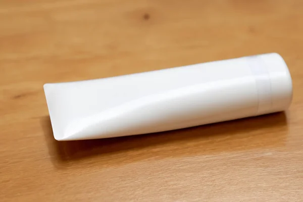 white cosmetic tube with cream on a wooden table, close - up