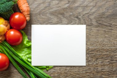 Tahta zemin üzerinde taze sebzelerle dolu boş bir kağıt.