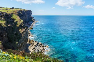 Mavi denizi ve güneşli bir günde dalgaları olan kayalık bir sahil.