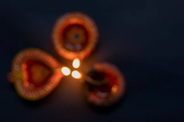 Happy Diwali. Dim three clay diya lamps lit against a black background. Hindu festival of lights.