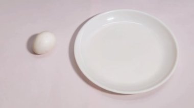 Beyaz arka planda hareket eden ve beyaz bir tabakta kırılan bir yumurtanın hareketini durdurun..
