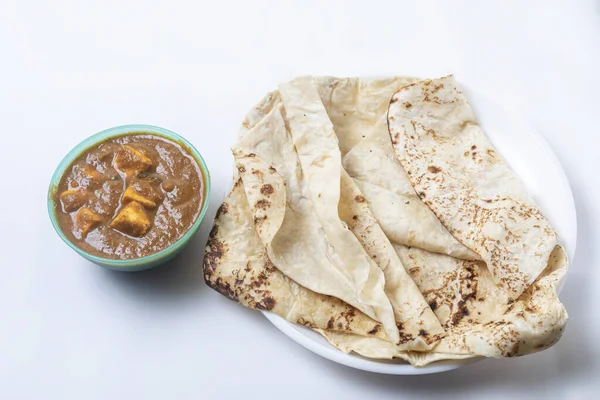 Popular Indian food on white background served with butter masala curry in a bowl with delicious butter naan on white plate. Top view.