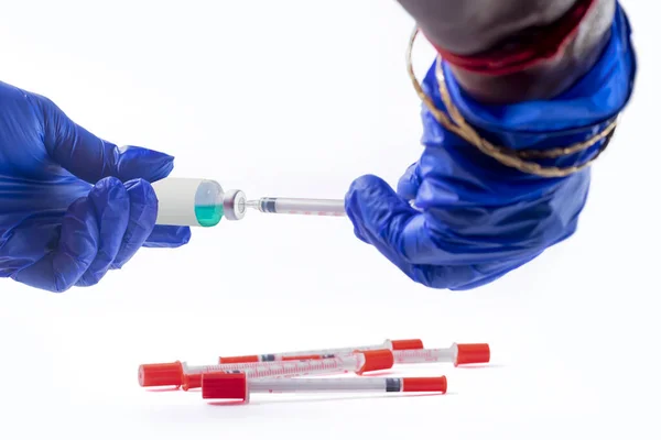 医師の手で青い手袋を保持注射器で緑のワクチンボトル いくつかの注射器が横たわっている — ストック写真