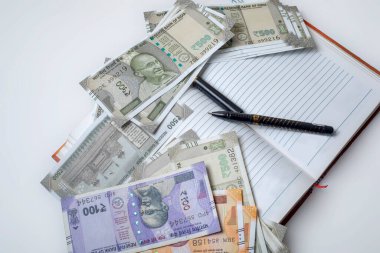 Beyaz bir arka planda açık bir defter üzerinde kalemle Hindistan banknotları.