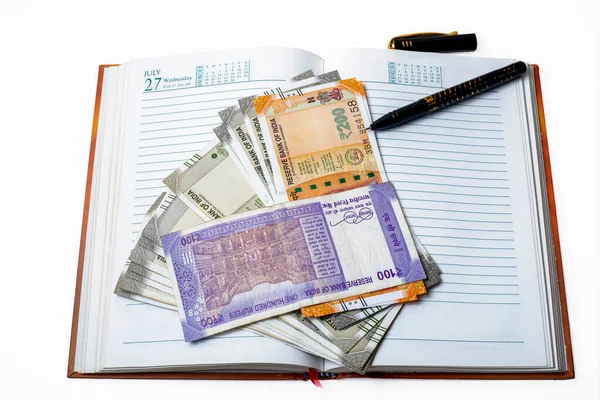 Save money concept. pile of Indian money with pen over open notebook on a white background.