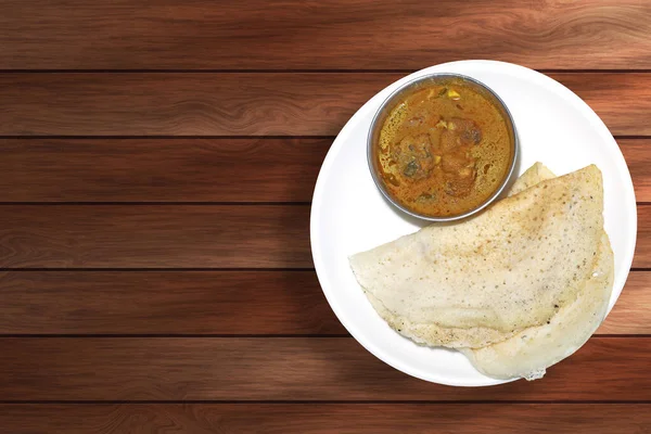 Ahşap arka planda beyaz tabakta tavuk körili dosa manzarası.