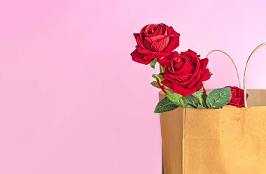 Yapay kırmızı güller pembe arka planda kese kağıdında. Sevgililer Günü konsepti.
