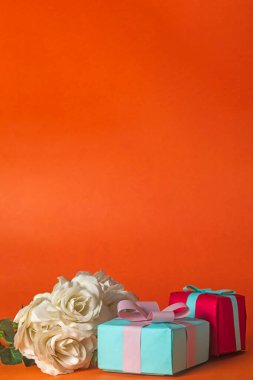 Sevgililer Günü konsepti: hediye kutuları ve turuncu arka planda beyaz güller. Boşluğu kopyala.