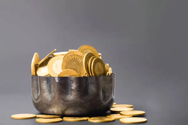 Golden coins in a copper bowl on a dark background with copy space