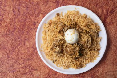 Tavuk biryani, ortasında yumurta olan popüler bir Hint yemeğidir. Beyaz tabakta servis edilen lezzetli biryani tavuğunun üst görüntüsü. Kapat..