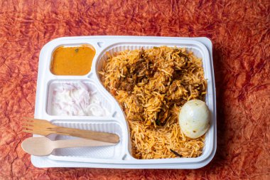 Hint tavuk biryanisi raita, et suyu ve ahşap masada tahta kaşıkla dolu beyaz plastik bir kutuda. Yakın çekim