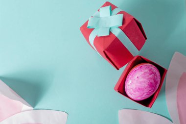 Hediye kutusunda Paskalya yumurtası ve mavi arka planda tavşan kulağı. Üst görünüm