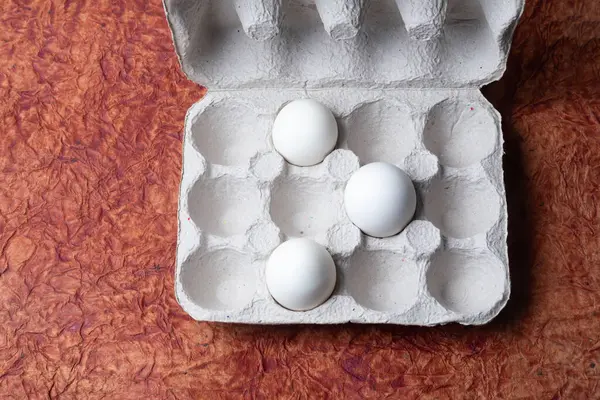 White eggs in a carton box on a brown textured paper background. Top view.
