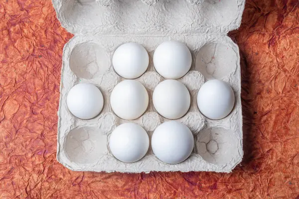 White eggs in a carton box on a brown textured paper background. Top view.