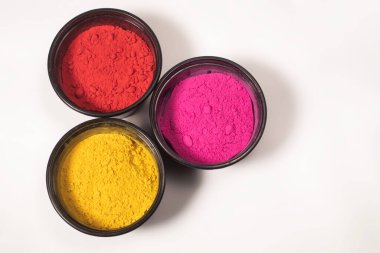 Parlak kırmızı, pembe ve sarı renkli Holi tozlu üç küçük plastik kutu, temiz beyaz bir arka plana karşı, Hint Renk Festivali.