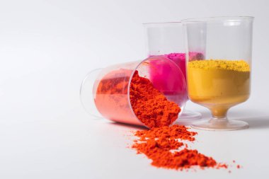 Fotokopi alanı olan beyaz bir arkaplan üzerindeki ölçüm bardaklarında renkli holi tozu