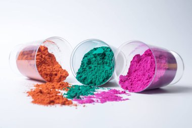Beyaz arka planda izole edilmiş cam bir kabın içindeki renkli holi tozu. Holi festivali.