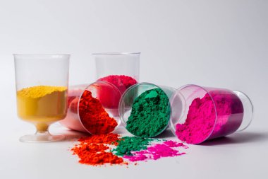 Beyaz arka planda izole edilmiş cam bir kabın içindeki renkli holi tozu. Holi festivali.