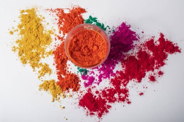 Beyaz arka planda kırmızı holi tozu ve etrafa saçılmış çok renkli holi tozları. Üst görünüm.