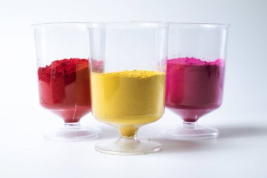 Beyaz arka planda izole edilmiş bir bardakta çok renkli holi tozu. Holi pudrası geleneksel bir Hint festivalidir. Yakın çekim.